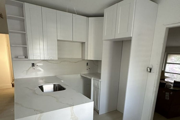 Modern kitchen with sleek white cabinetry, marble countertops, and a built-in sink, featuring an open layout and natural light.