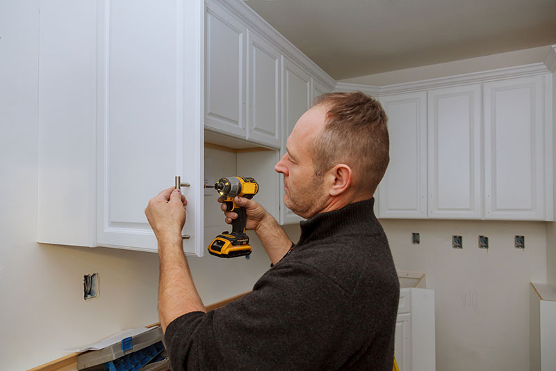 A contractor using a drill for precise cabinet installation.