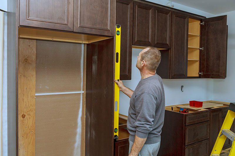 A professional installer using a level to check the alignment of kitchen cabinets during a cabinet installation project.