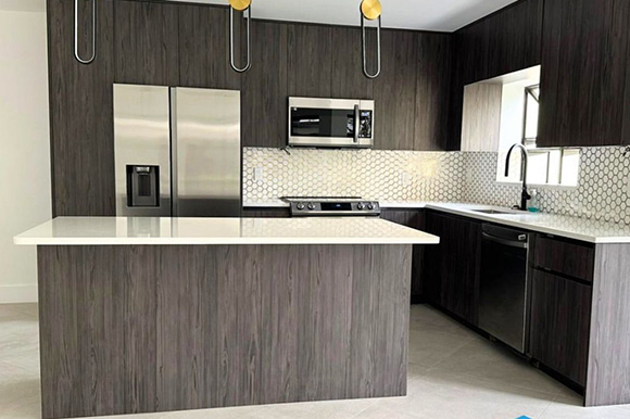 Modern kitchen featuring dark wood cabinetry, stainless steel appliances, a white quartz countertop, and hexagon tile backsplash.